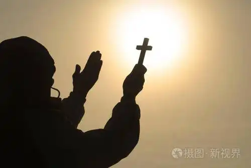 基督教男子的剪影,手中拿着十字架,祈祷上帝在阳光