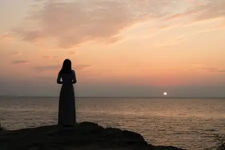 一个女孩在日落背景(日出)上的剪影在海平线上. 夏天在海滩上散步.