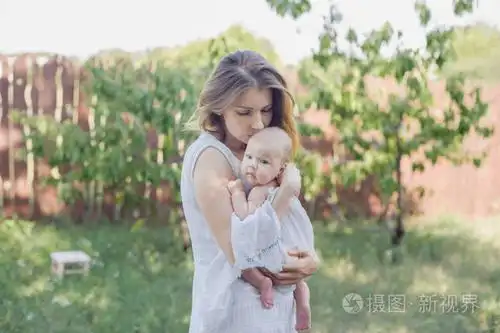 一个美丽的年轻母亲抱着一个婴儿在她的怀里站在花园里