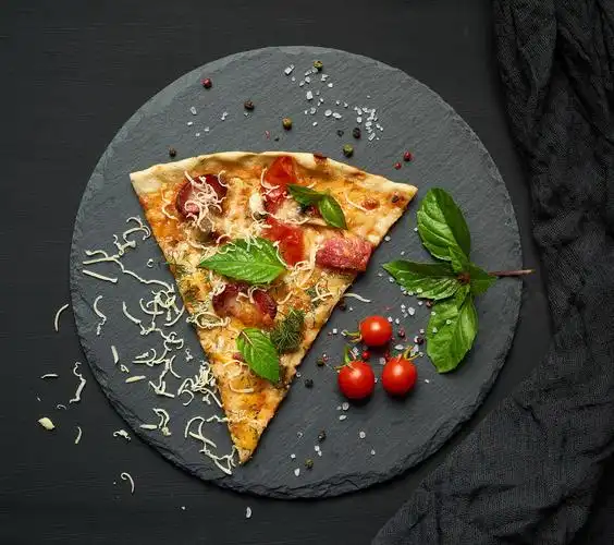 美味的三角形披萨片上面有熏香肠蘑菇西红柿奶酪和罗勒叶放在黑色石墨