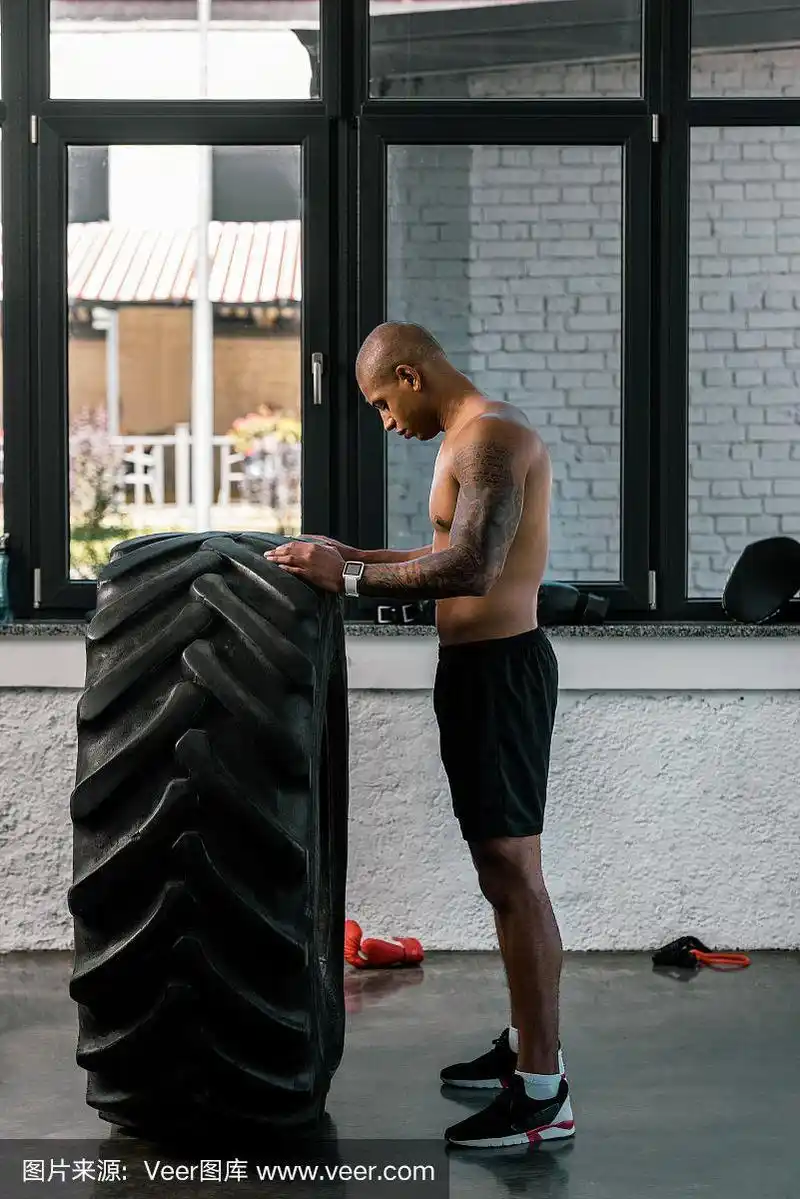 侧视图肌肉裸男训练与轮胎在健身房