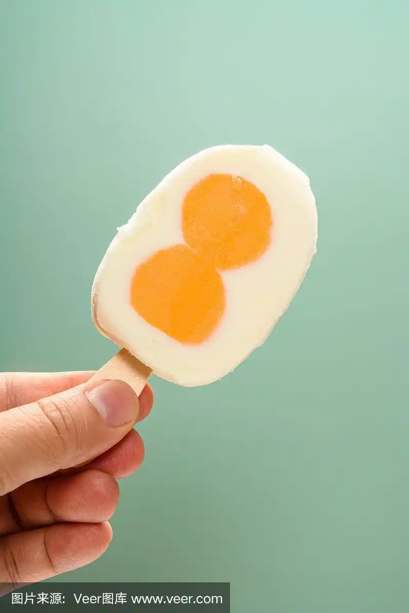 手拿一个新鲜的鸡蛋形状的冰棒在绿色的背景