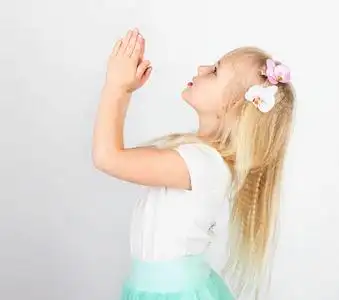 金发碧眼的小女孩双手合十祈祷上帝.一个小天使.侧面视图照片