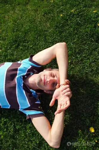 一个年轻人快乐轻松的用手在头下的草地上的肖像照片-正版商用图片0