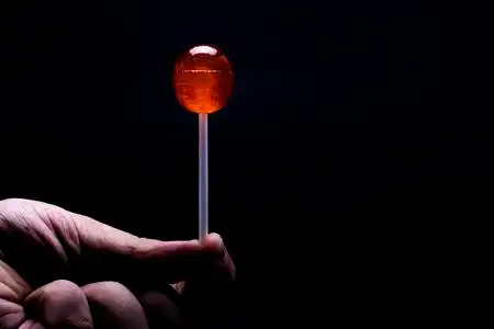 一只棒棒糖一只手拿着红色棒棒糖,黑色背景照片