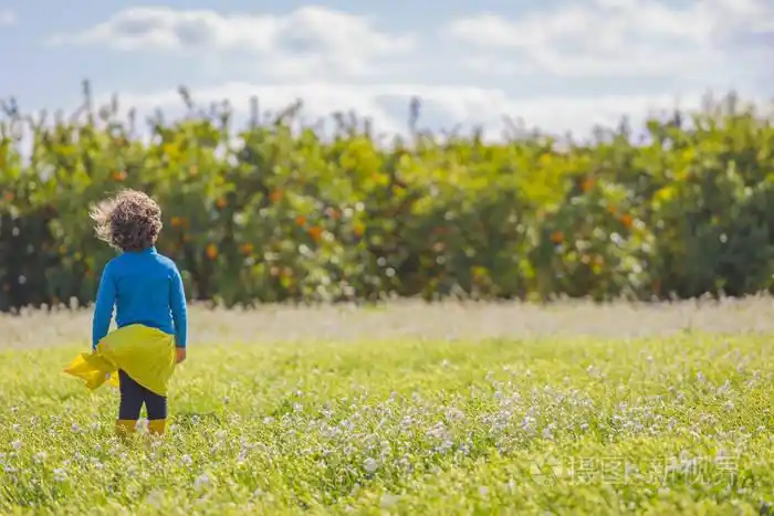在阳光明媚的日子里, 穿着黄色短裙和蓝色运动衫的小漂亮女孩在绿色