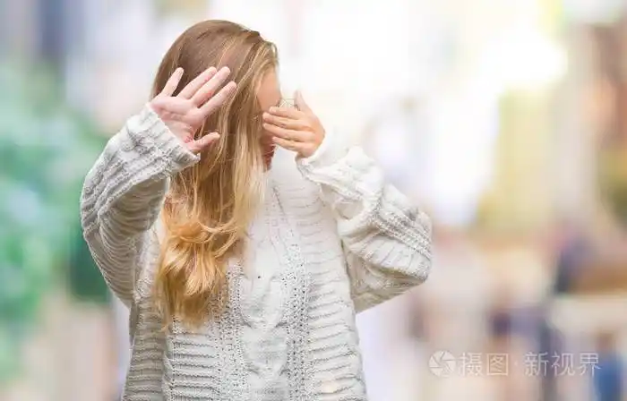 漂亮的金发女人穿着冬天的毛衣和太阳镜,在孤立的背景上用手遮住眼睛