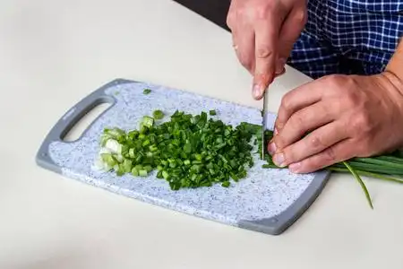 鲜葱片.在厨房里煮蔬菜.男人手拿刀,在白色桌子上的菜板上切蔬菜.照片