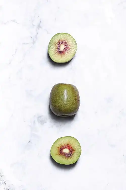 放在白色大理石上的切开的红心猕猴桃平铺背景图片下载