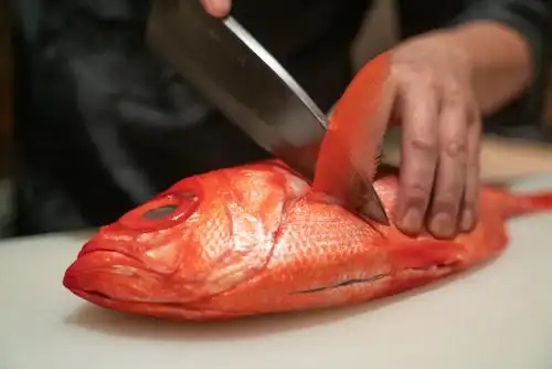 正在用刀处理一整条红色金目鲷鱼食材