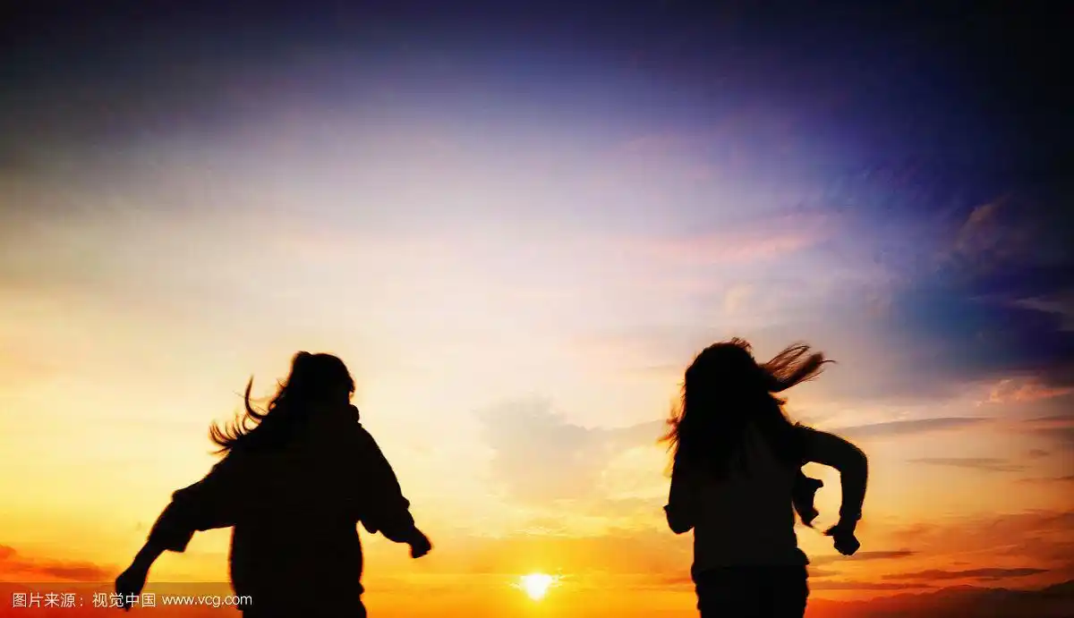 两个女人在日落的海滩上跑步的照片