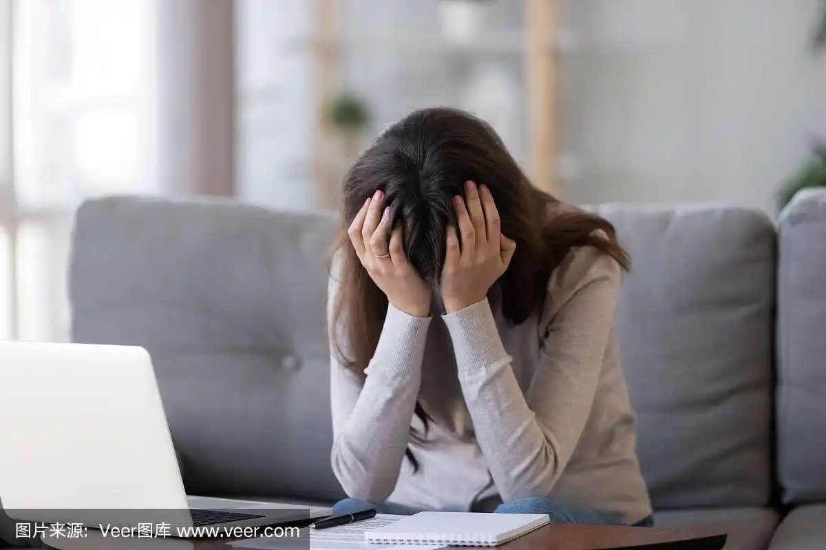心烦意乱的女人双手抱头沮丧地坐在笔记本电脑附近
