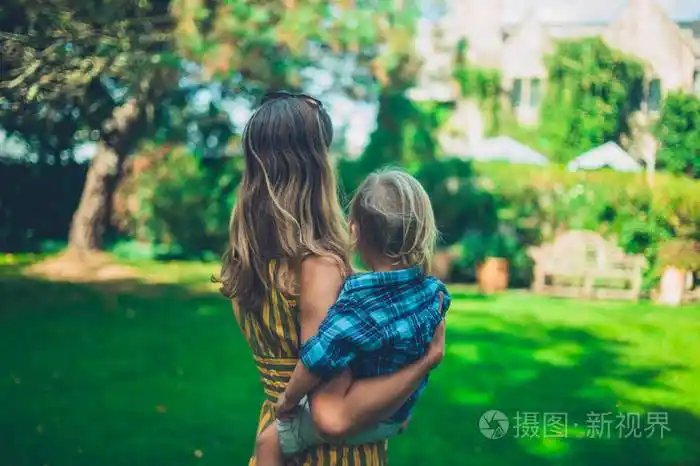 一位母亲抱着她的蹒跚学步的孩子在郁郁葱葱的乡村花园里