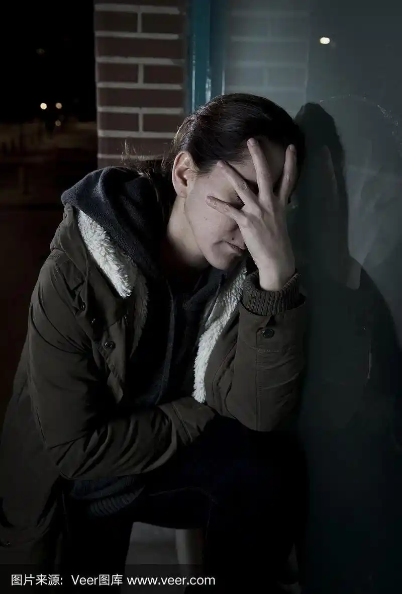 悲伤沮丧的女人独自在夜晚靠在街道的窗户上
