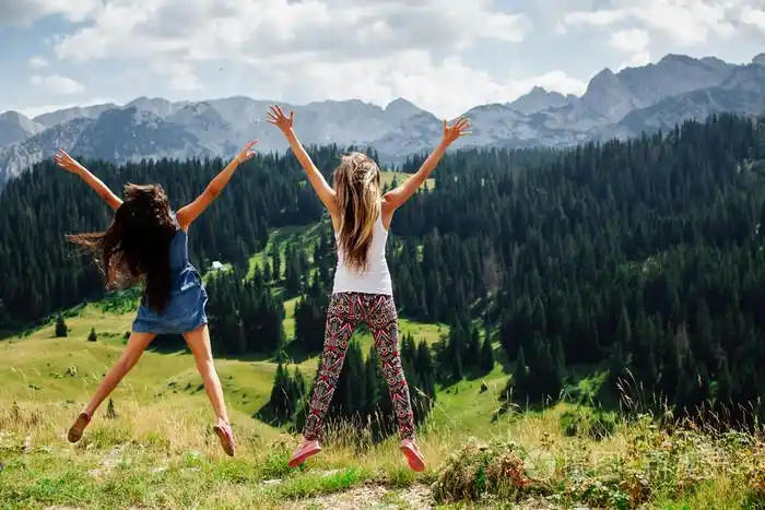 两个女孩在山背视图中快乐地跳起来