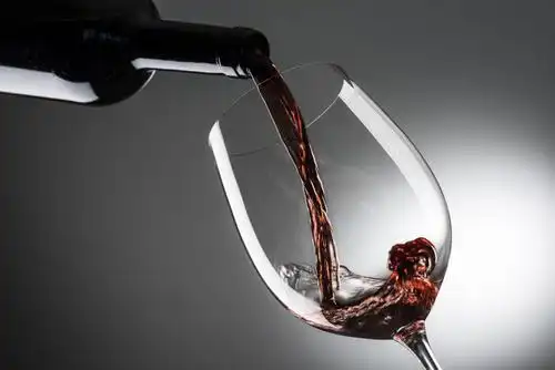 日落时分的葡萄园背景下向高脚杯中倒入红酒