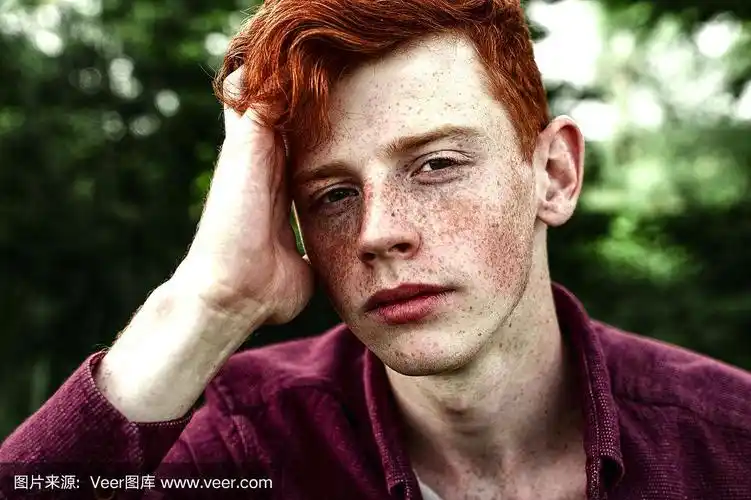 这是一幅有魅力的时尚青年模特的肖像,红头发,雀斑坐在绿色的草地上