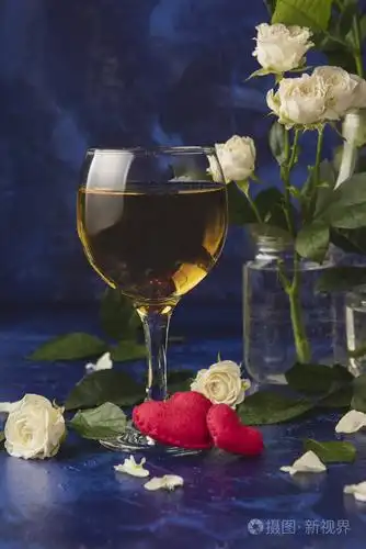 情人节白葡萄酒浪漫的夜晚一杯酒一束白色玫瑰和红色的心蓝色背景上有