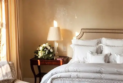 卧室里,简约的床品旁一个木制床头柜静立在旁以及一盘软装植物展现了