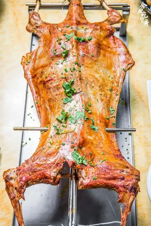 烤全羊一整匹羊被拉平固定在烤架上,炭火燃烧,翻转着烤熟,再经过刷油