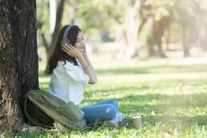 年轻的亚洲休闲时髦女孩听音乐在城市公园